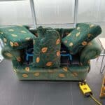 A green sofa with floral patterns being cleaned with air dryers placed on the cushions to aid drying.