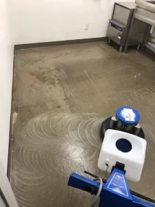 Commercial kitchen floor being professionally cleaned with a floor scrubbing machine.