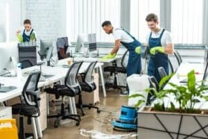 Professional cleaning team performing office cleaning, including floor scrubbing and surface sanitization, in a modern workspace.