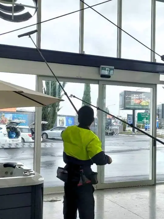 Professional window cleaner using an extended pole system to clean high glass panels inside a commercial building.