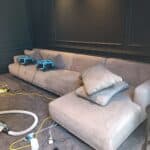 A grey sofa being cleaned with specialized equipment, with air dryers placed on the cushions to ensure fast drying.