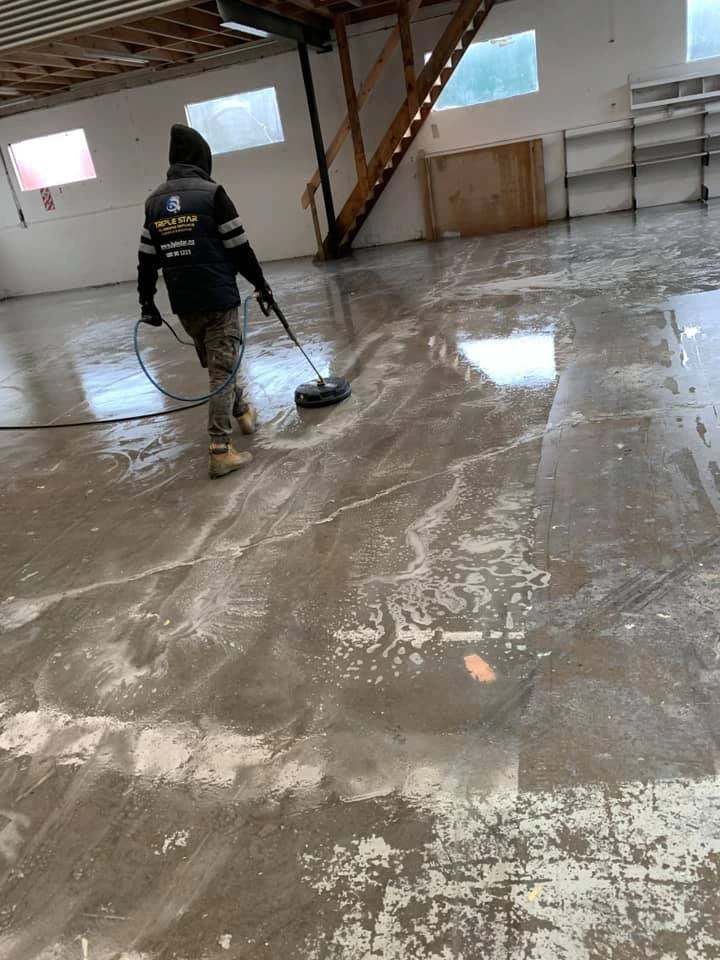 Professional cleaner using a pressure washing machine to clean a large concrete floor in an industrial space.