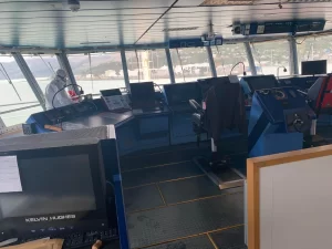 Professional cleaner in protective gear disinfecting a ship's control bridge using specialized sanitization equipment.