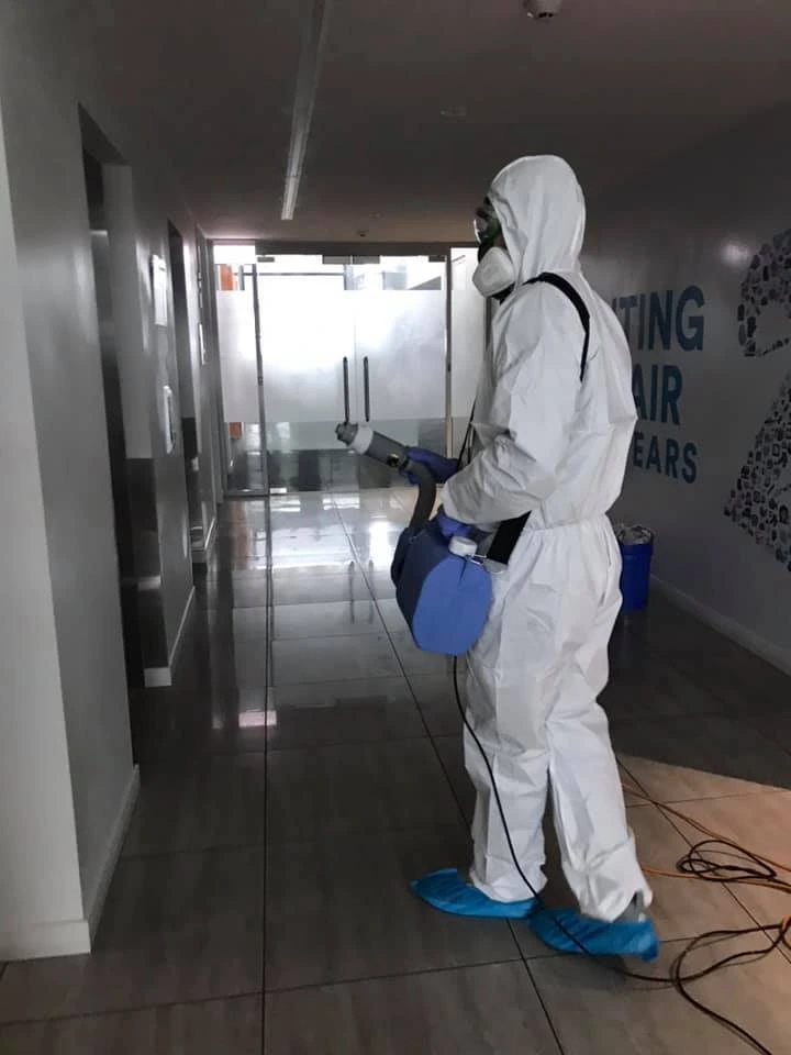 Professional cleaner in full protective gear disinfecting a commercial building hallway with specialized equipment.