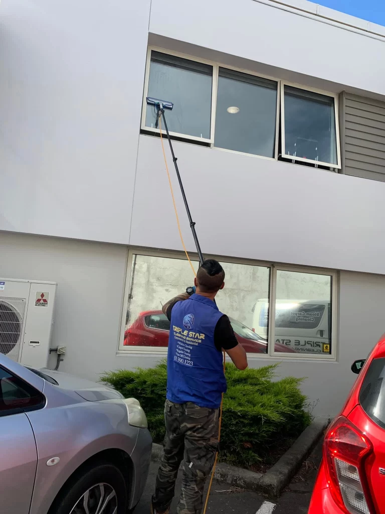 Professional window cleaner using an extended water-fed pole system to clean second-story exterior windows of a commercial building.