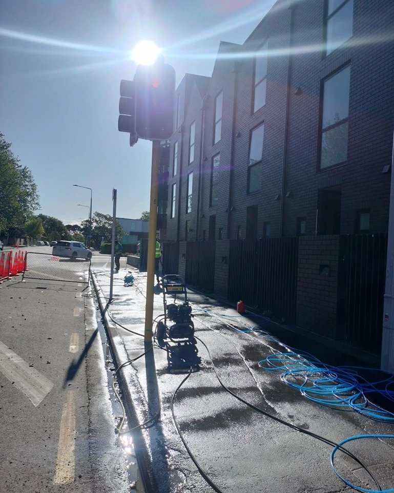 Professional pressure washing service being performed on a residential sidewalk and building exterior under bright sunlight.