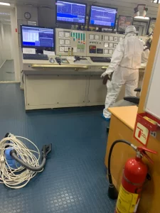 Professional cleaner in full protective gear sanitizing a control room with specialized disinfecting equipment.