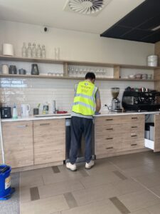 Commercial kitchen cleaning with worker in high-visibility vest